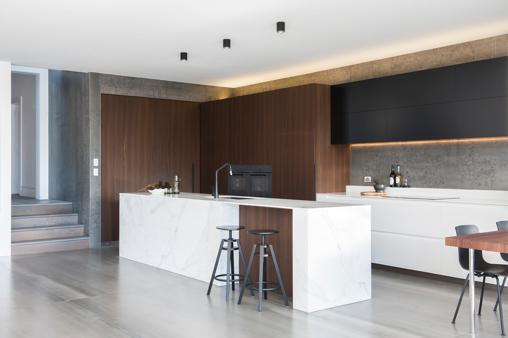 Photo of a mid-sized modern l-shaped eat-in kitchen in Sydney with an integrated sink, dark wood cabinets, solid surface benchtops, grey splashback, cement tile splashback, black appliances, ceramic floors and with island.
