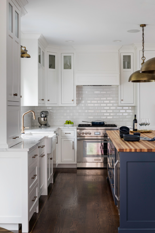 Design ideas for a mid-sized transitional l-shaped eat-in kitchen in Boston with a farmhouse sink, recessed-panel cabinets, white cabinets, quartzite benchtops, white splashback, subway tile splashback, stainless steel appliances, medium hardwood floors, with island and white benchtop.