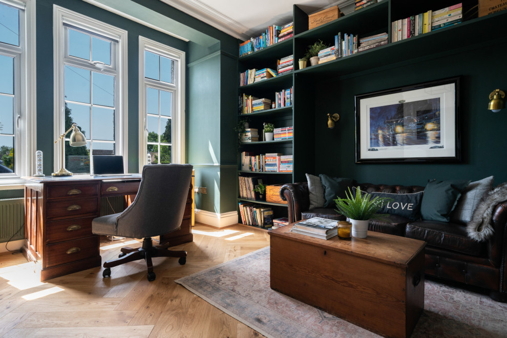 Ejemplo de despacho actual de tamaño medio con paredes verdes, suelo vinílico, todas las chimeneas, marco de chimenea de yeso y escritorio independiente