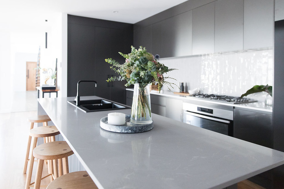 Inspiration for a mid-sized modern galley open plan kitchen in Canberra - Queanbeyan with a double-bowl sink, black cabinets, quartz benchtops, grey splashback, subway tile splashback, black appliances, medium hardwood floors, with island and brown floor.