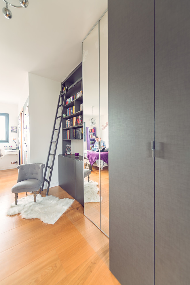 This is an example of a mid-sized industrial women's built-in wardrobe in Rennes with grey cabinets, light hardwood floors and flat-panel cabinets.