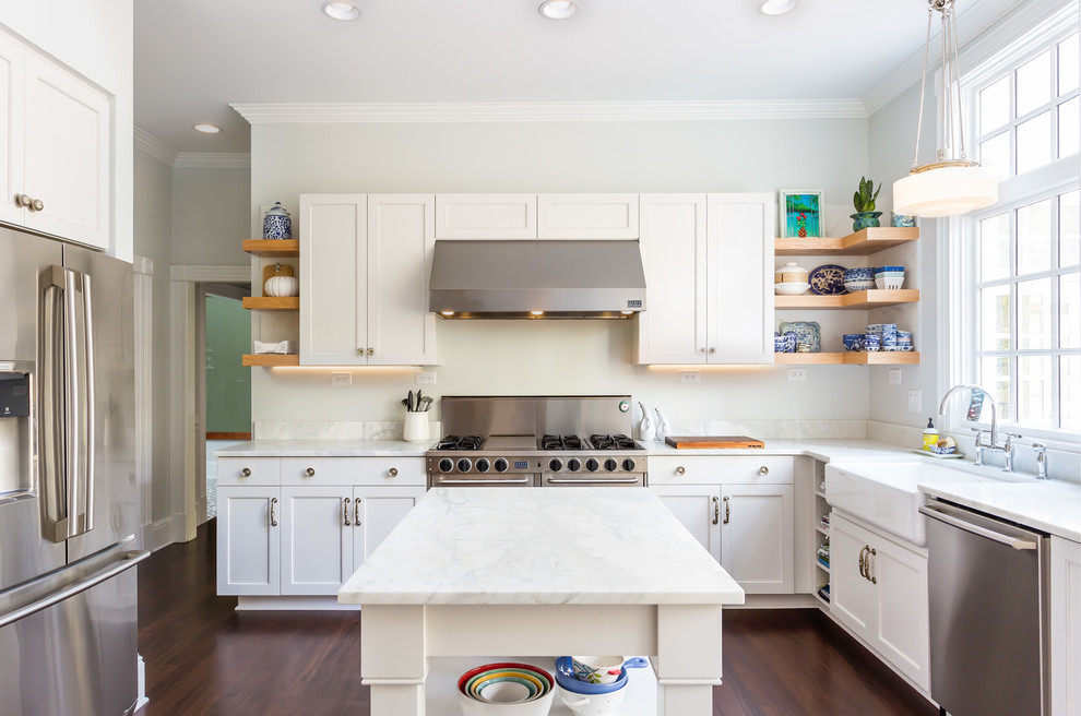 Design ideas for a large transitional u-shaped kitchen in Raleigh with a farmhouse sink, shaker cabinets, white cabinets, stainless steel appliances, dark hardwood floors, with island, marble benchtops, white splashback, marble splashback, brown floor and white benchtop.