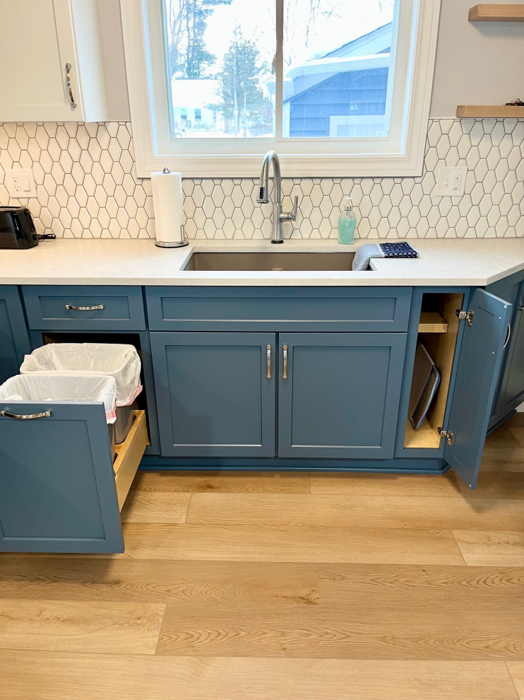 Mid-sized transitional u-shaped vinyl floor and brown floor eat-in kitchen photo with an undermount sink, shaker cabinets, white cabinets, quartz countertops, white backsplash, ceramic backsplash, stainless steel appliances, no island and white countertops