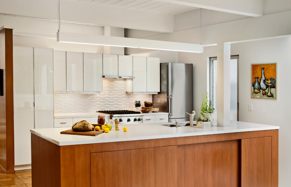 This is an example of a midcentury galley kitchen in San Francisco with stainless steel appliances, flat-panel cabinets, white cabinets and white splashback.
