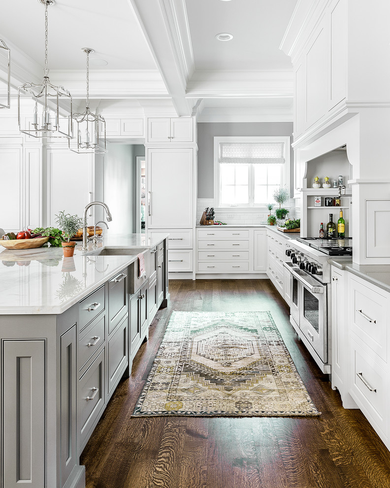 Photo of a large transitional kitchen in Chicago with a farmhouse sink, beaded inset cabinets, white cabinets, white splashback, ceramic splashback, stainless steel appliances, with island, brown floor and dark hardwood floors.