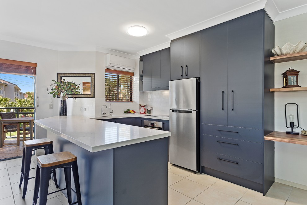 This is an example of a contemporary u-shaped kitchen in Gold Coast - Tweed with an undermount sink, flat-panel cabinets, blue cabinets, white splashback, stone tile splashback, stainless steel appliances and a peninsula.