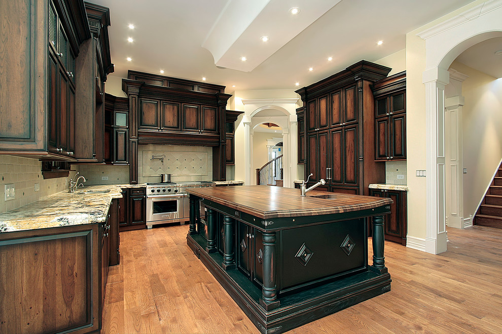 Large transitional u-shaped light wood floor eat-in kitchen photo with raised-panel cabinets, granite countertops, beige backsplash, stone tile backsplash, an undermount sink, dark wood cabinets, paneled appliances and an island