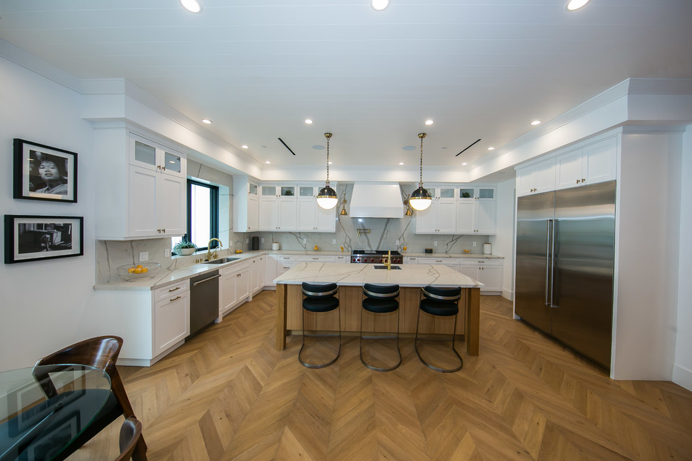 This is an example of a large modern u-shaped eat-in kitchen in Los Angeles with a drop-in sink, raised-panel cabinets, white cabinets, granite benchtops, white splashback, granite splashback, stainless steel appliances, porcelain floors, with island, beige floor, white benchtop and wood.