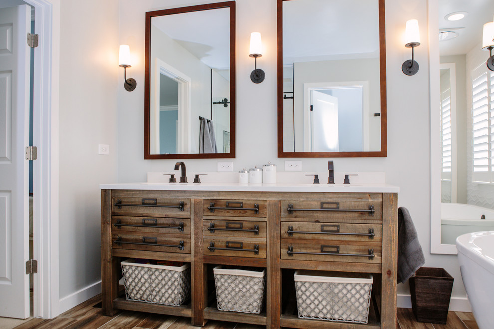 Photo of a mid-sized country master bathroom in Denver with furniture-like cabinets, distressed cabinets, a freestanding tub, an alcove shower, a one-piece toilet, white tile, ceramic tile, grey walls, porcelain floors, an undermount sink, engineered quartz benchtops, brown floor and a sliding shower screen.