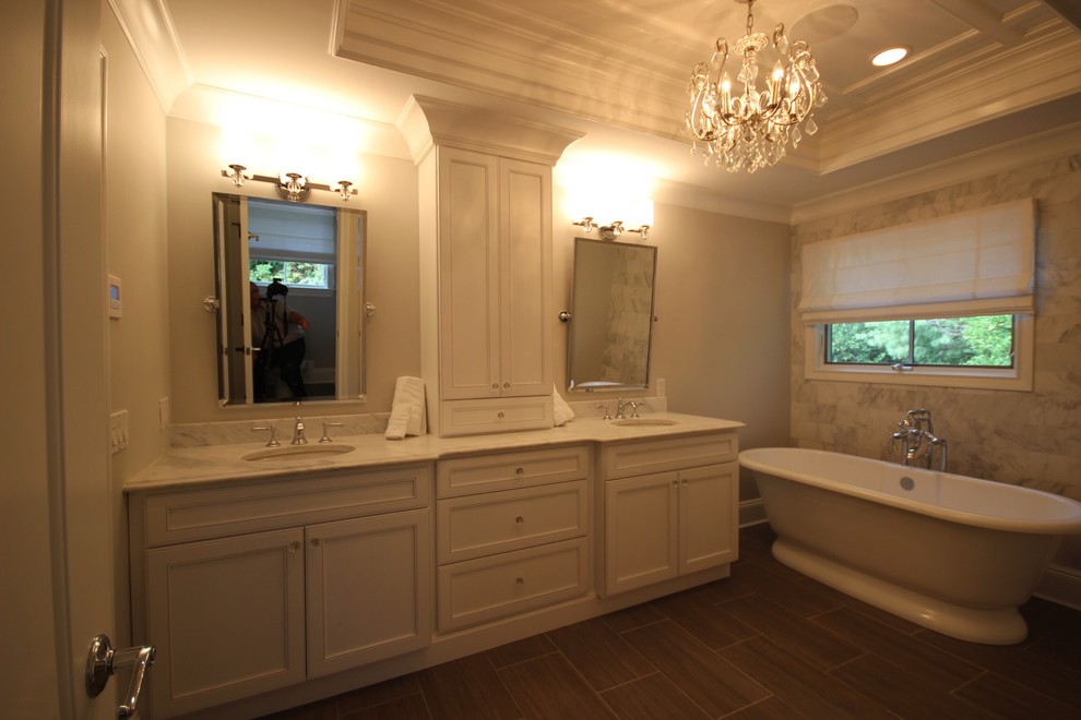 This is an example of a large transitional master bathroom in New York with recessed-panel cabinets, white cabinets, a freestanding tub, a corner shower, a one-piece toilet, beige walls, porcelain floors, an undermount sink and marble benchtops.