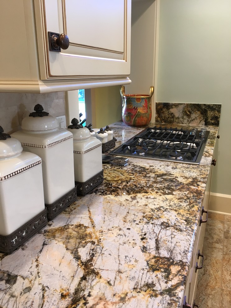 Enclosed kitchen - large transitional galley porcelain tile enclosed kitchen idea with an undermount sink, raised-panel cabinets, distressed cabinets, granite countertops, beige backsplash, stone tile backsplash, stainless steel appliances and a peninsula