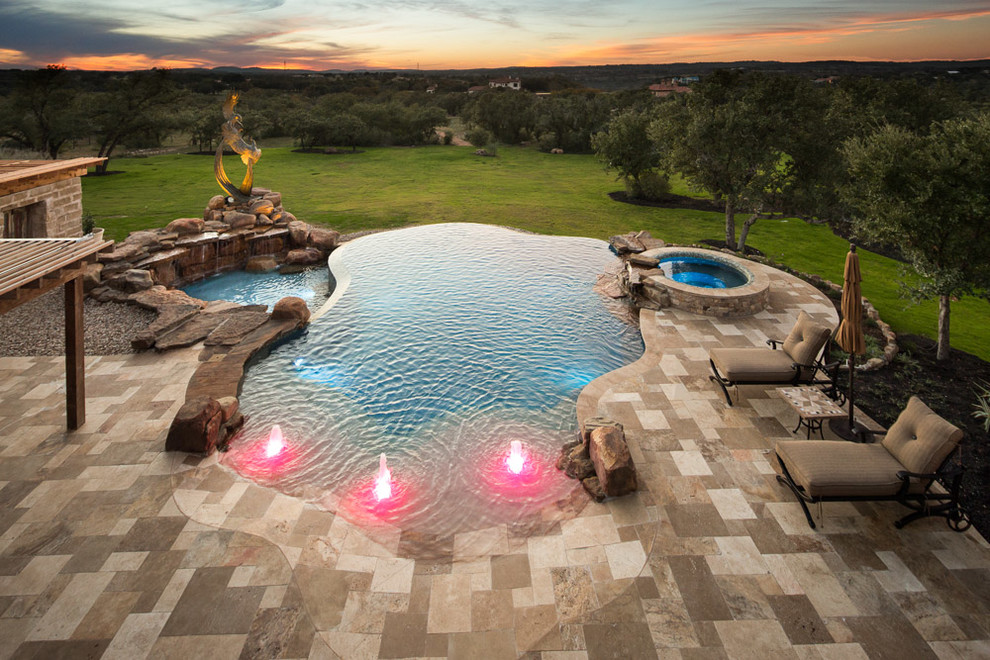 This is an example of an expansive traditional backyard custom-shaped infinity pool in Austin with natural stone pavers.
