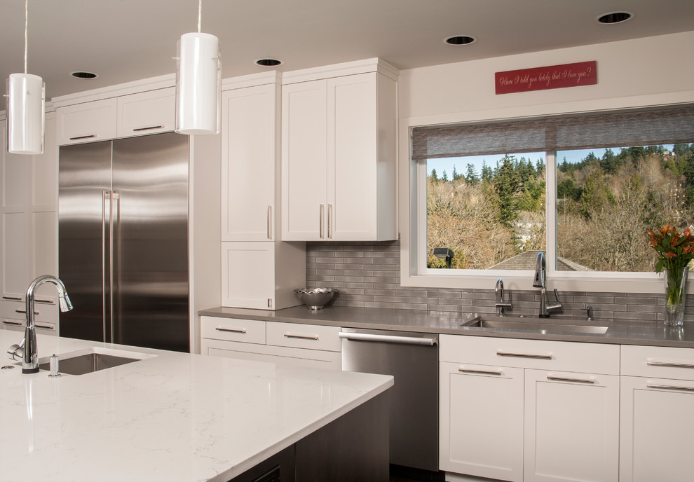This is an example of a large contemporary kitchen in Seattle with recessed-panel cabinets, white cabinets, quartz benchtops, grey splashback, stainless steel appliances, medium hardwood floors, with island and brown floor.