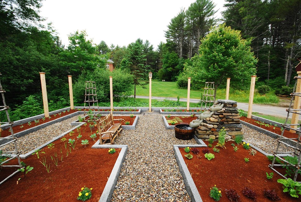 Large traditional backyard full sun formal garden in Portland Maine with a vegetable garden and river rock for summer.