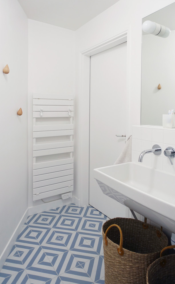 Minimalistisk inredning av ett litet vit vitt badrum med dusch, med en dusch i en alkov, en toalettstol med separat cisternkåpa, vit kakel, keramikplattor, vita väggar, mellanmörkt trägolv, ett väggmonterat handfat, beiget golv och dusch med gångjärnsdörr