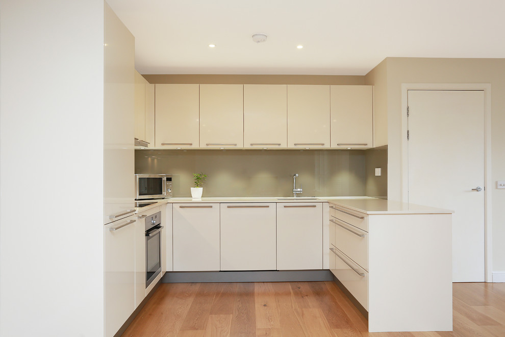 Photo of a mid-sized modern u-shaped open plan kitchen in London with glass-front cabinets, glass sheet splashback, a peninsula and stainless steel appliances.