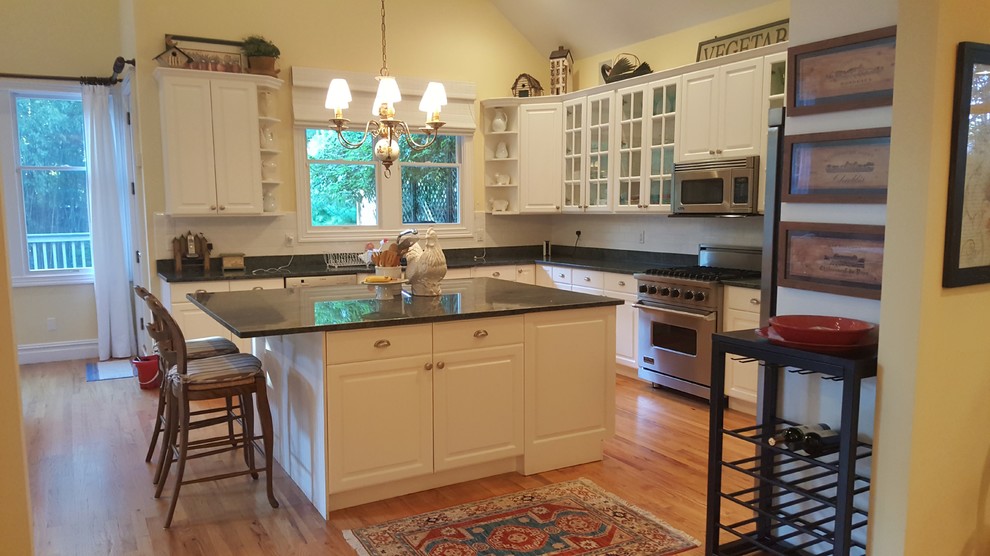 Inspiration for a mid-sized country galley eat-in kitchen in New York with glass-front cabinets, white cabinets, granite benchtops, white splashback, ceramic splashback, stainless steel appliances, light hardwood floors, with island and green benchtop.