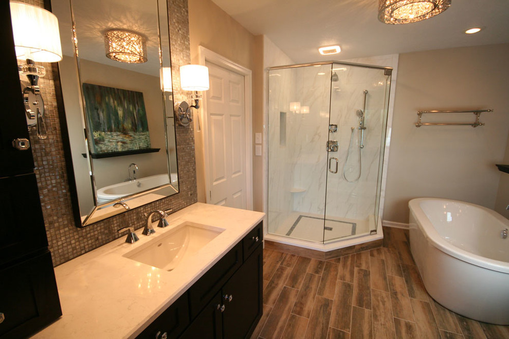 Mid-sized transitional master bathroom in Other with beige walls, a freestanding tub, a corner shower, an undermount sink, quartzite benchtops, flat-panel cabinets, dark wood cabinets, gray tile, mosaic tile, laminate floors, brown floor, a hinged shower door and white benchtops.