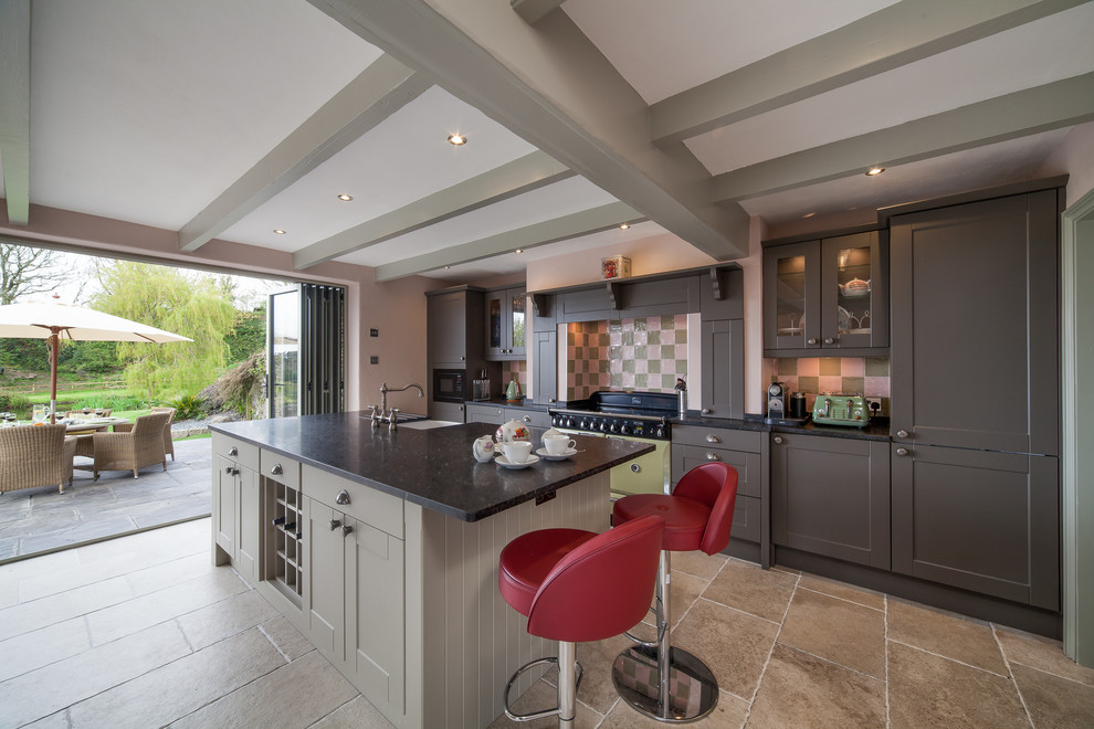 Inspiration for a mid-sized traditional single-wall kitchen in Cornwall with a farmhouse sink, recessed-panel cabinets, granite benchtops, multi-coloured splashback, ceramic splashback, with island, brown floor, black benchtop, grey cabinets and panelled appliances.