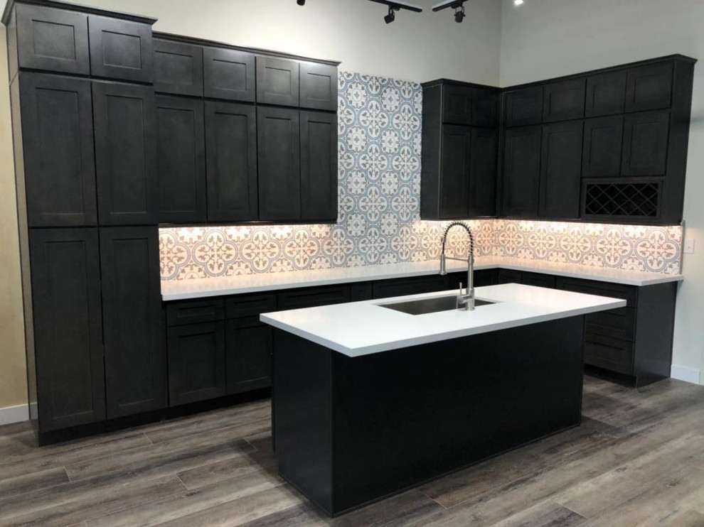 Design ideas for a mid-sized modern l-shaped kitchen in Las Vegas with a farmhouse sink, shaker cabinets, white cabinets, quartz benchtops, grey splashback, glass tile splashback, stainless steel appliances, vinyl floors, multiple islands, brown floor and white benchtop.