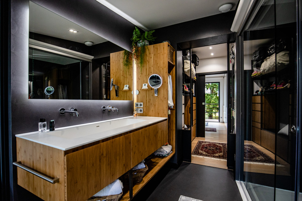 This is an example of an eclectic bathroom in Toulouse with flat-panel cabinets, medium wood cabinets, black tile, black walls, a trough sink, black floor, white benchtops, a double vanity and a floating vanity.
