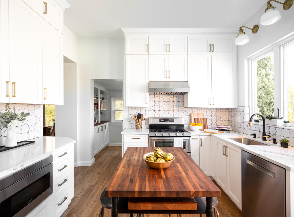 Design ideas for a large transitional u-shaped separate kitchen in Denver with an undermount sink, white cabinets, white splashback, ceramic splashback, stainless steel appliances, medium hardwood floors, with island, white benchtop, recessed-panel cabinets and brown floor.