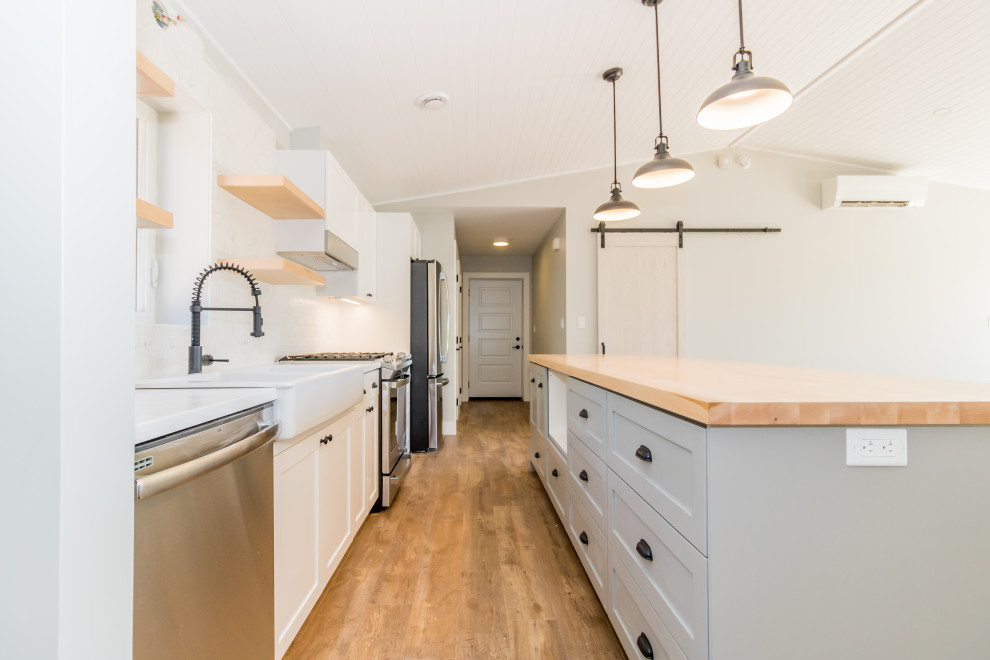 Example of a mid-sized galley vinyl floor and brown floor kitchen design with a farmhouse sink, recessed-panel cabinets, white cabinets, quartzite countertops, stainless steel appliances, an island and multicolored countertops