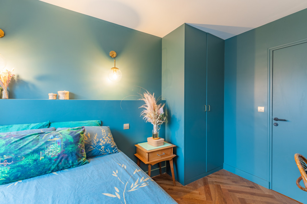 Cette image montre une chambre parentale design de taille moyenne avec un mur bleu, parquet foncé, aucune cheminée, un sol marron et dressing.