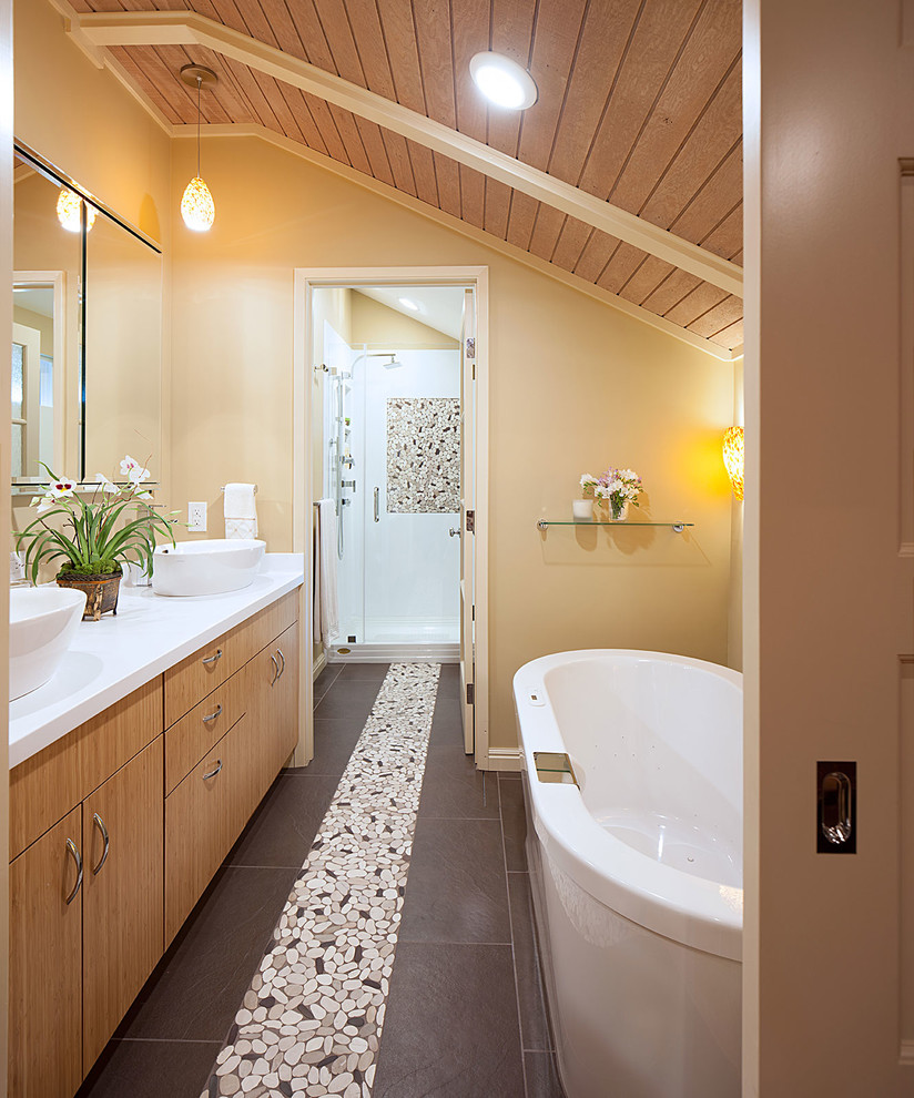 Photo of a large beach style master bathroom in San Francisco with a vessel sink, flat-panel cabinets, medium wood cabinets, solid surface benchtops, a freestanding tub, an alcove shower, a two-piece toilet, brown tile, porcelain tile, yellow walls and porcelain floors.