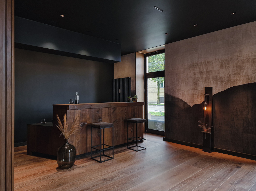 Photo of a mid-sized modern single-wall wet bar in Munich with dark wood cabinets, solid surface benchtops, brown splashback, timber splashback, painted wood floors, brown floor, black benchtop and flat-panel cabinets.