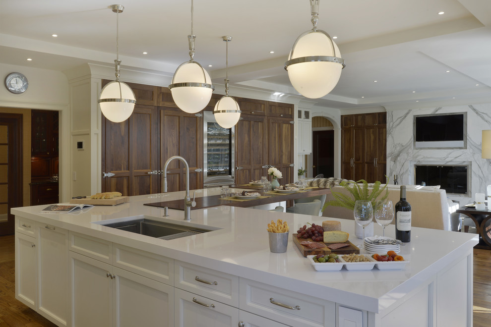 Example of a large transitional l-shaped medium tone wood floor and brown floor open concept kitchen design in New York with an undermount sink, shaker cabinets, white cabinets, quartzite countertops, white backsplash, marble backsplash, paneled appliances and an island