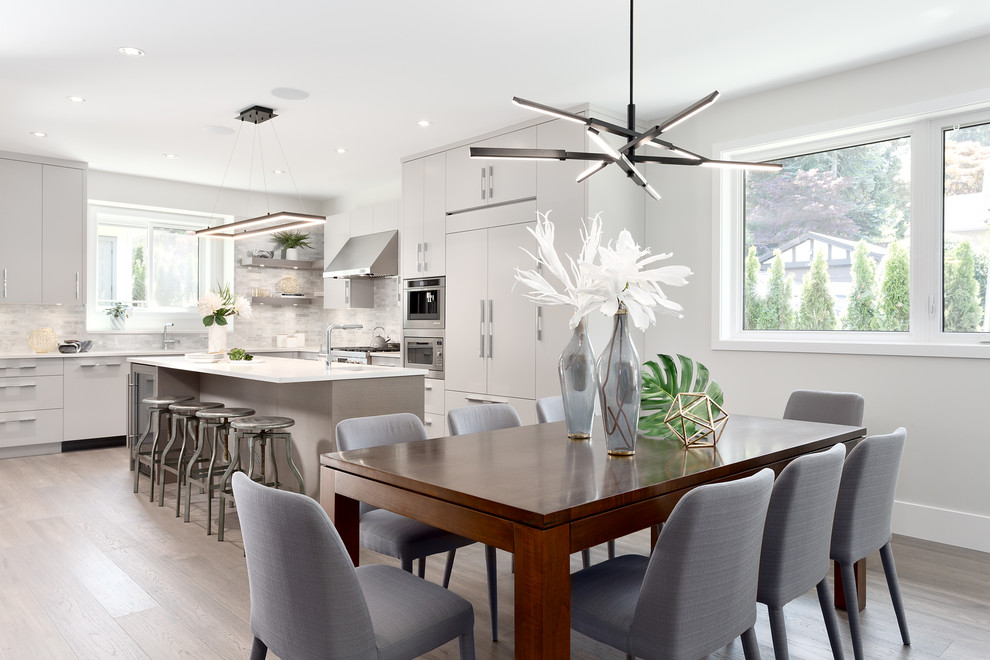 Photo of a mid-sized contemporary l-shaped open plan kitchen in Vancouver with medium hardwood floors, brown floor, a double-bowl sink, flat-panel cabinets, grey cabinets, solid surface benchtops, white splashback, stone tile splashback, panelled appliances, with island and white benchtop.