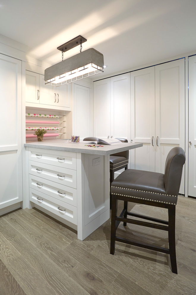 Mid-sized transitional l-shaped utility room in Toronto with recessed-panel cabinets, white cabinets, solid surface benchtops, light hardwood floors and a concealed washer and dryer.