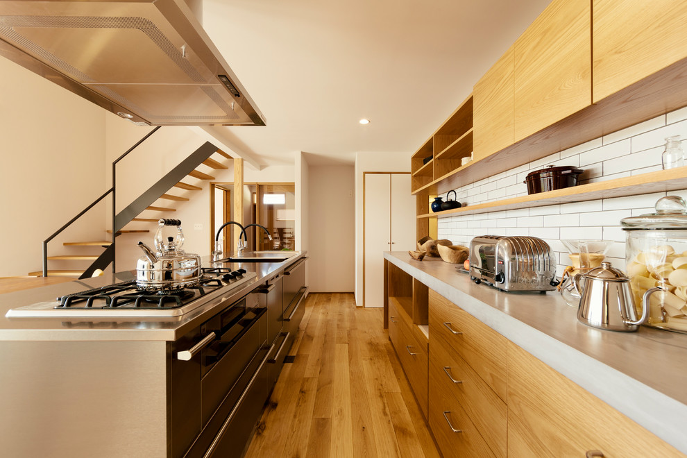 Design ideas for an asian galley kitchen in Other with an undermount sink, flat-panel cabinets, medium wood cabinets, stainless steel benchtops, white splashback, medium hardwood floors, with island, brown floor and grey benchtop.