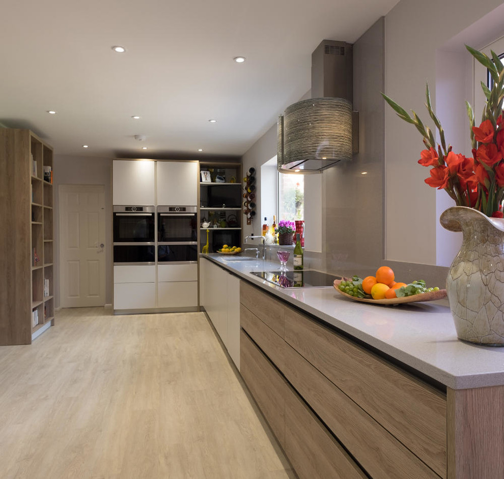 Photo of a mid-sized contemporary l-shaped open plan kitchen in Hampshire with an undermount sink, flat-panel cabinets, medium wood cabinets, quartzite benchtops, grey splashback, stone slab splashback, stainless steel appliances, light hardwood floors and grey benchtop.