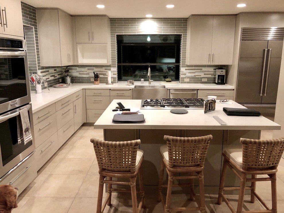 Example of a large transitional l-shaped porcelain tile and beige floor enclosed kitchen design with a farmhouse sink, flat-panel cabinets, white cabinets, quartz countertops, gray backsplash, subway tile backsplash, stainless steel appliances, an island and white countertops