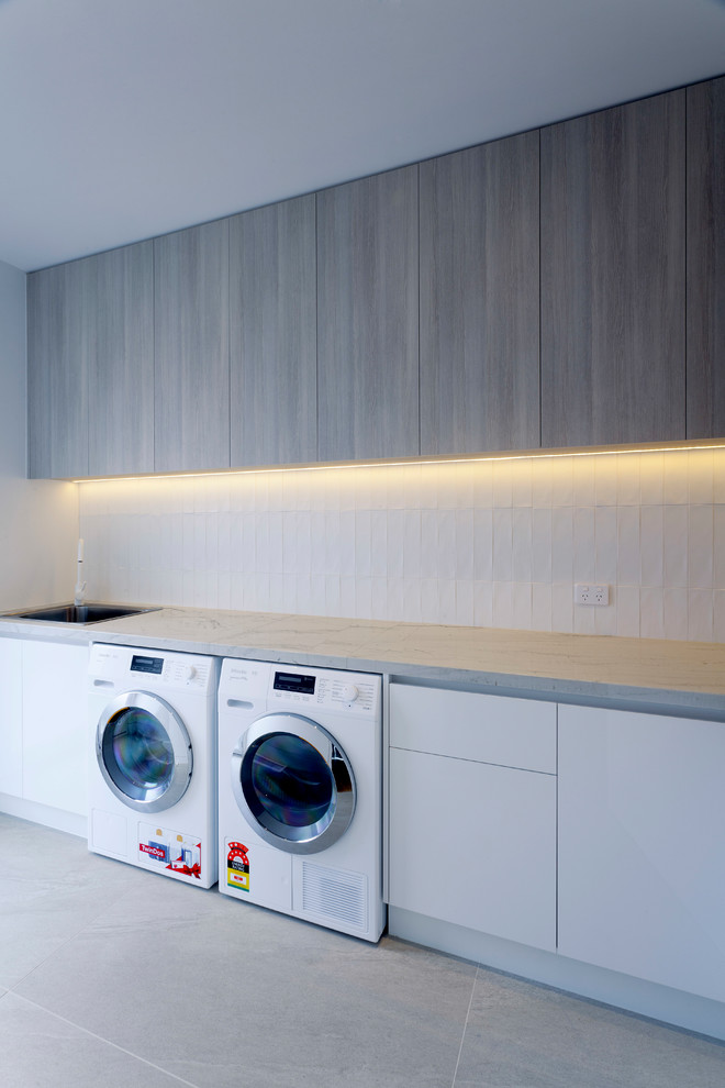 Photo of a large modern l-shaped laundry room in Melbourne with a drop-in sink, flat-panel cabinets, distressed cabinets, quartzite benchtops, a side-by-side washer and dryer and grey benchtop.
