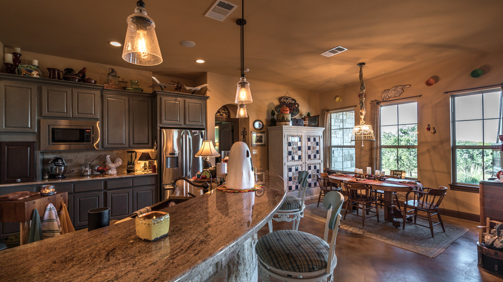 Eat-in kitchen - large rustic l-shaped concrete floor eat-in kitchen idea in Austin with a farmhouse sink, shaker cabinets, gray cabinets, granite countertops, beige backsplash, subway tile backsplash, stainless steel appliances and an island
