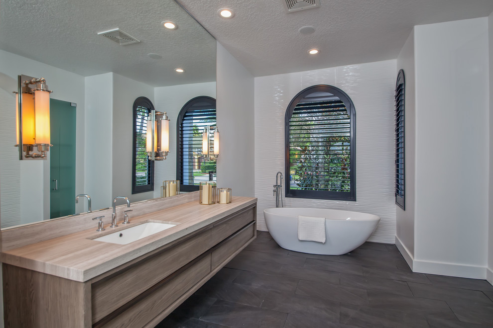 Photo of a mid-sized contemporary master bathroom in Miami with flat-panel cabinets, medium wood cabinets, a freestanding tub, white tile, white walls, an undermount sink, grey floor, an alcove shower, ceramic tile, slate floors, engineered quartz benchtops and a hinged shower door.