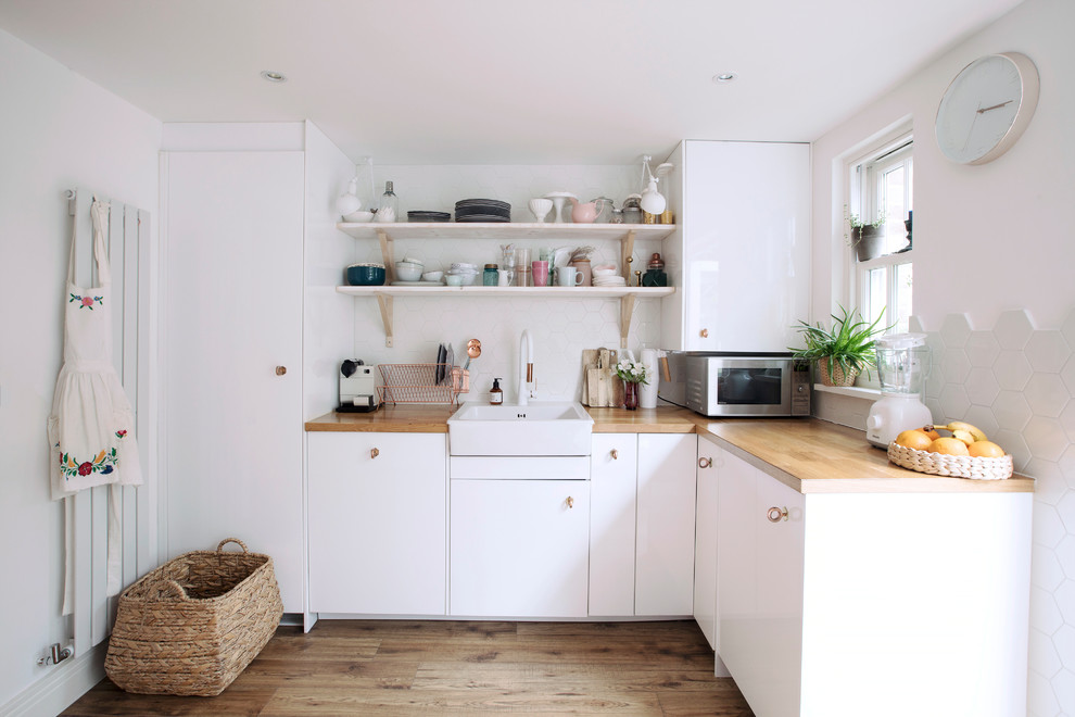 Inspiration for a scandinavian l-shaped kitchen in London with a farmhouse sink, flat-panel cabinets, white cabinets, wood benchtops, white splashback, no island, brown floor and brown benchtop.