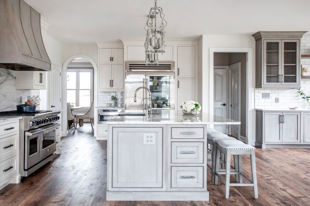 Inspiration for a l-shaped kitchen in Nashville with a farmhouse sink, beaded inset cabinets, grey cabinets, grey splashback, stone slab splashback, stainless steel appliances, dark hardwood floors, with island, brown floor and white benchtop.