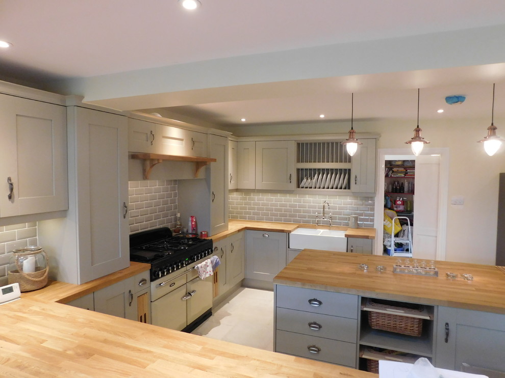 Large contemporary open plan kitchen in Cambridgeshire with a farmhouse sink, shaker cabinets, wood benchtops, ceramic splashback, coloured appliances, ceramic floors and with island.