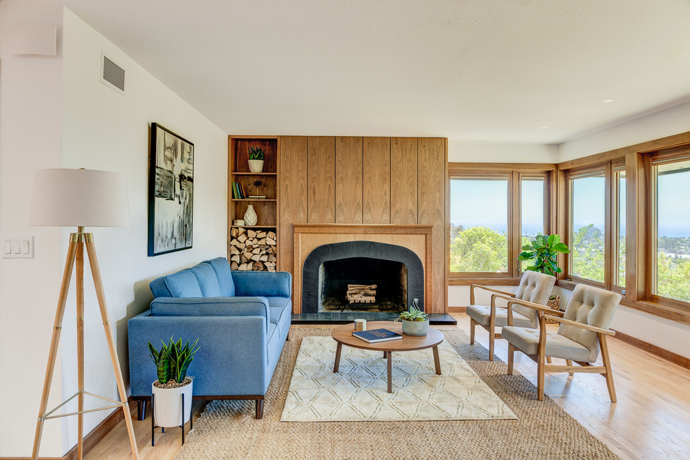 This is an example of a mid-sized midcentury formal open concept living room in San Francisco with white walls, light hardwood floors, a standard fireplace, a wood fireplace surround, no tv and brown floor.