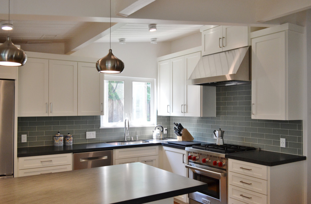 Photo of a small transitional l-shaped open plan kitchen in San Francisco with an undermount sink, shaker cabinets, white cabinets, granite benchtops, blue splashback, glass tile splashback, stainless steel appliances, medium hardwood floors, with island, black benchtop and exposed beam.