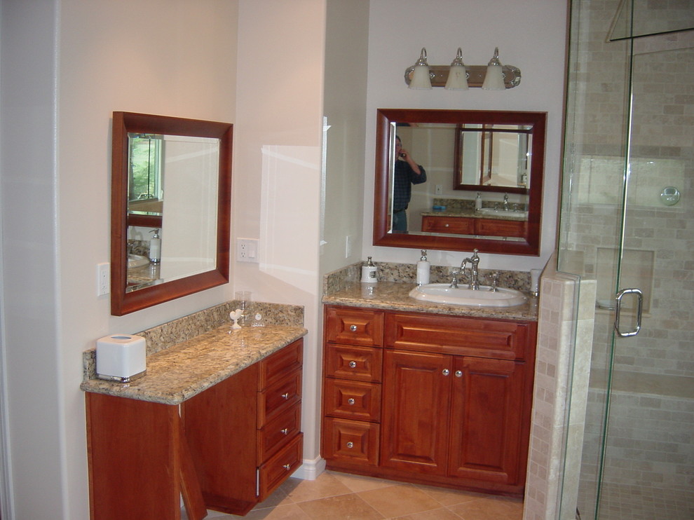 This is an example of a mid-sized traditional master bathroom in Orange County with raised-panel cabinets, medium wood cabinets, a freestanding tub, a corner shower, a two-piece toilet, gray tile, glass sheet wall, white walls, travertine floors, a drop-in sink and granite benchtops.