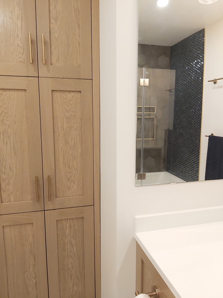 This is an example of a small classic bathroom in Ottawa with recessed-panel cabinets, medium wood cabinets, an alcove bath, a shower/bath combination, a one-piece toilet, blue tiles, glass tiles, white walls, porcelain flooring, a submerged sink, engineered stone worktops, multi-coloured floors, a hinged door, white worktops, a wall niche, a single sink and a floating vanity unit.