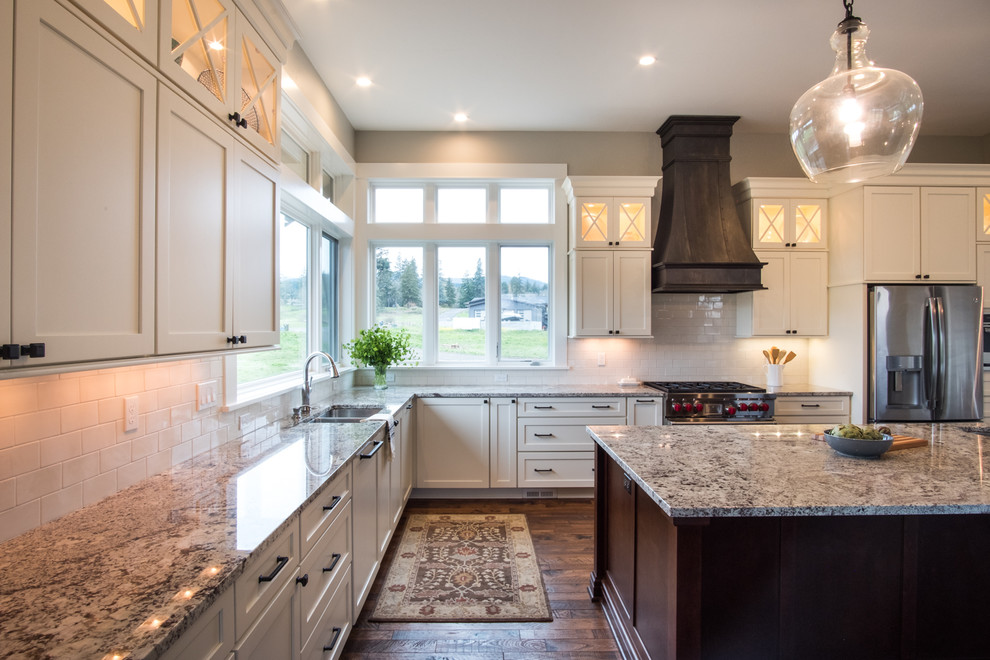 Large transitional l-shaped laminate floor and brown floor open concept kitchen photo in Portland with an undermount sink, shaker cabinets, white cabinets, quartz countertops, white backsplash, ceramic backsplash, stainless steel appliances, an island and multicolored countertops