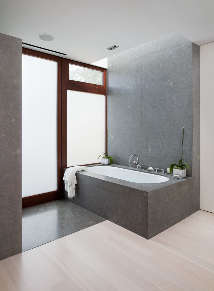 Photo of a contemporary bathroom in Los Angeles with an undermount tub, gray tile, stone slab, white walls and light hardwood floors.