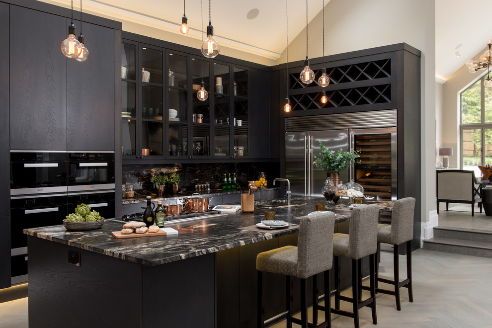 Inspiration for a large transitional galley open plan kitchen in London with black cabinets, stainless steel appliances, with island and light hardwood floors.