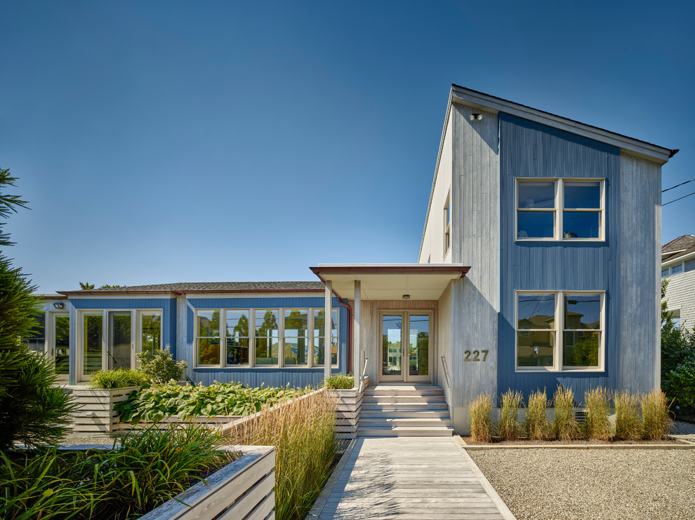 Beach style blue house exterior in New York with wood siding, a shingle roof and a shed roof.
